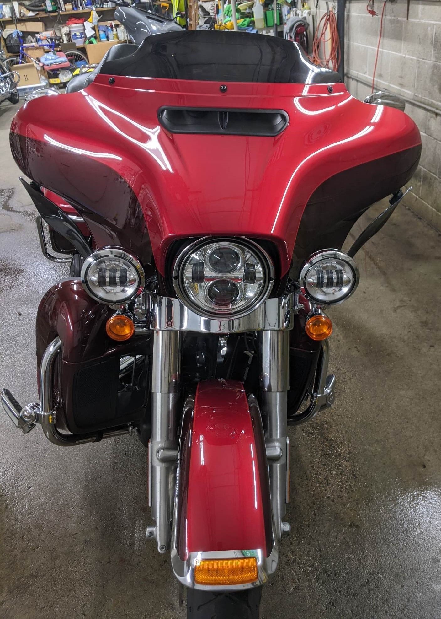 A front-facing view of a shiny, metallic red Harley-Davidson motorcycle with chrome accents, parked in a workshop.