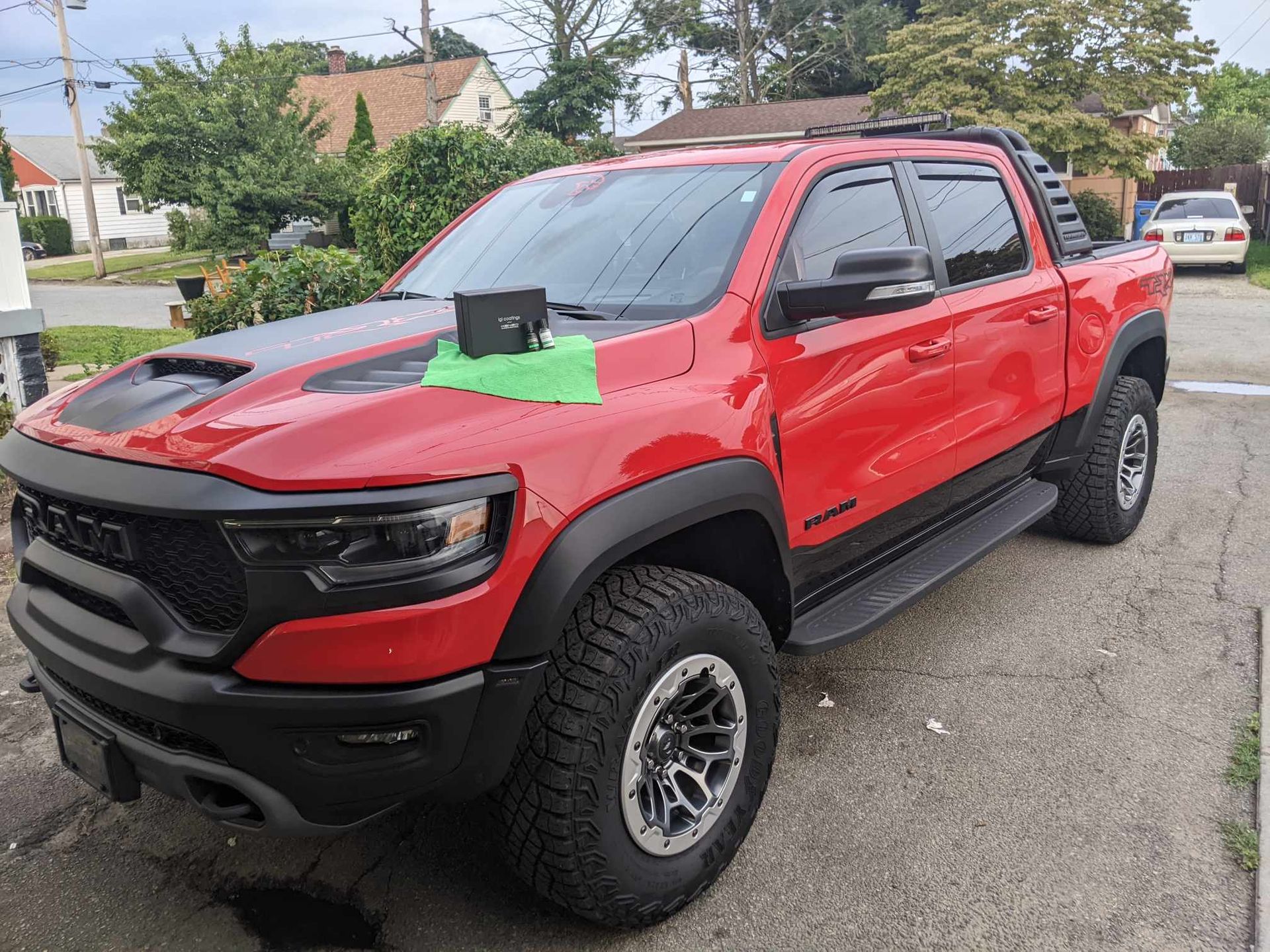 A bright red RAM TRX pickup truck parked on a residential street with a small box and green cloth on its hood.