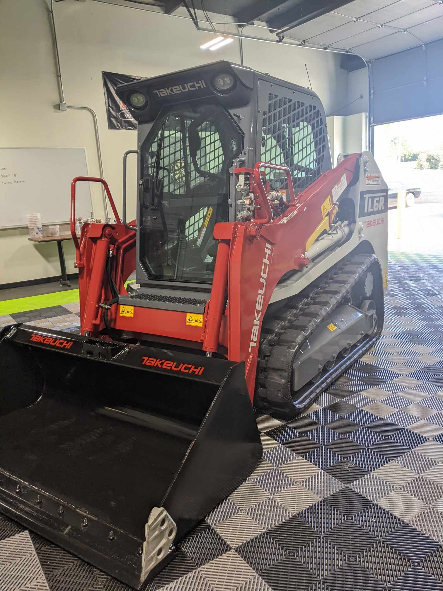 A red and white Takeuchi track loader with a large front bucket parked inside a building with a patterned floor.