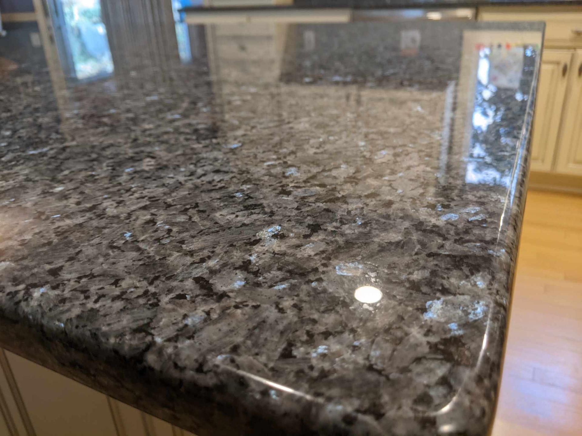 A close-up view of polished, dark blue-grey granite countertop with crystalline flecks, resting on white kitchen cabinets.