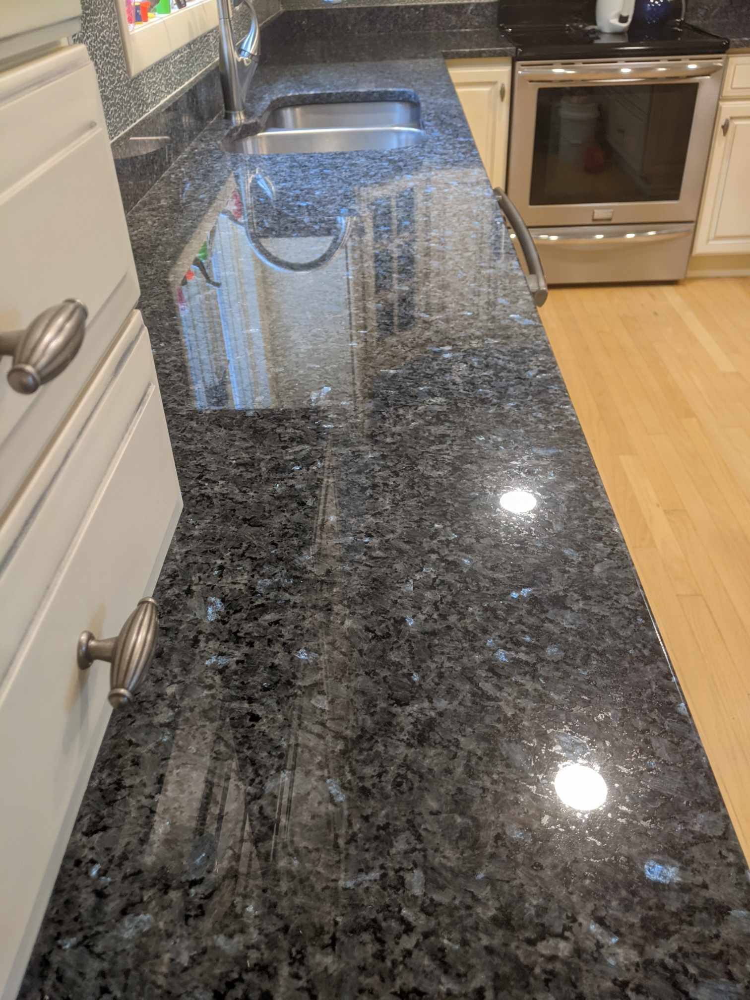 A close-up of a dark blue, granite countertop with a polished finish, next to a stainless steel sink and a range.