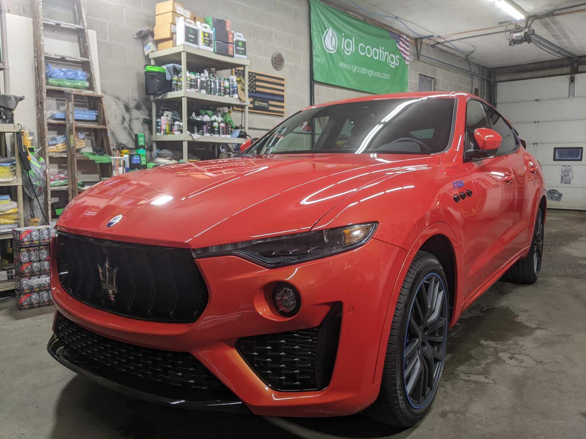 A bright orange Maserati SUV parked inside a garage, featuring a black grille, dark wheels, and a clean, polished finish.