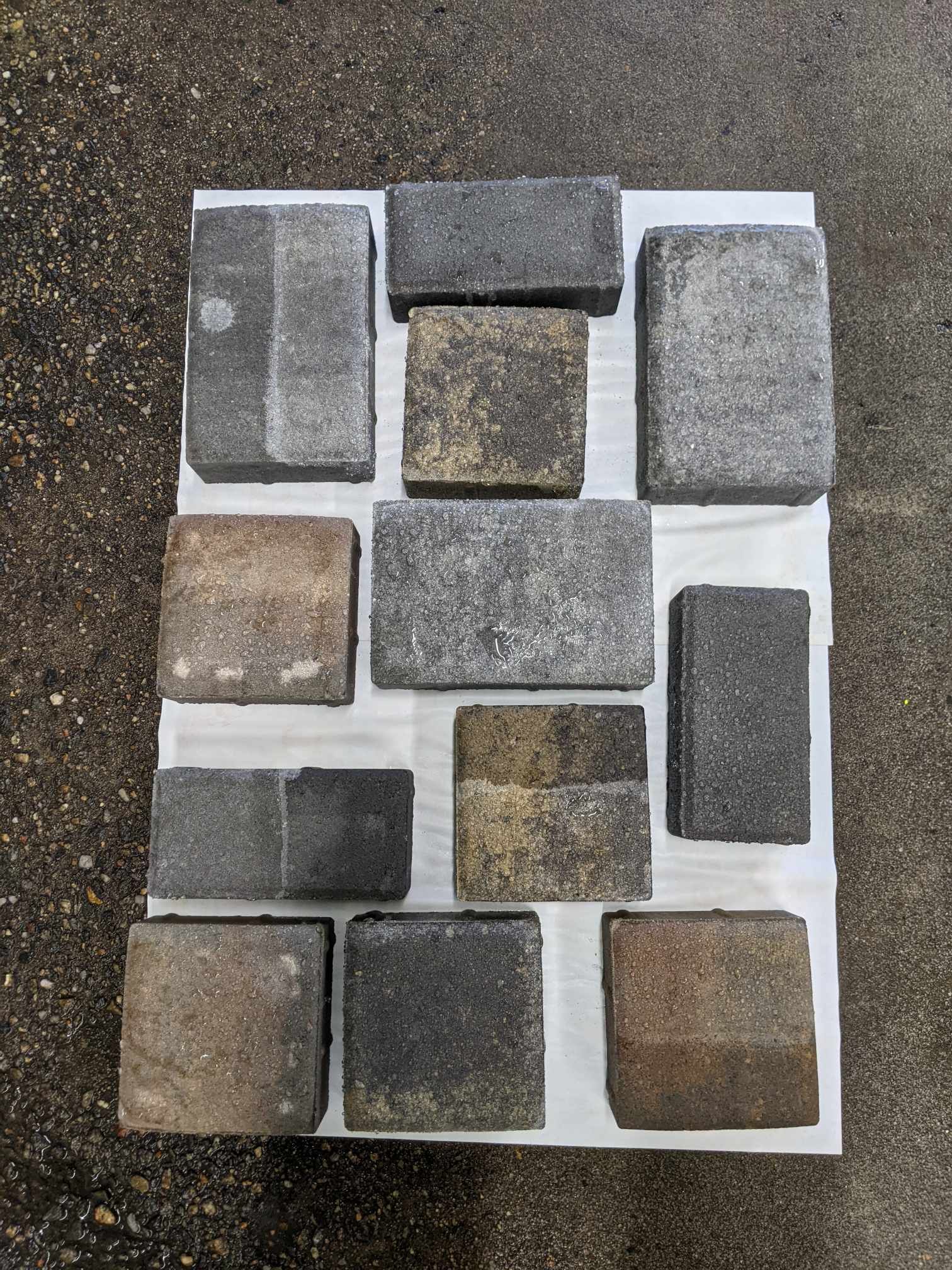 Twelve rectangular and square stone pavers in varying shades of gray and brown arranged on a white sheet.