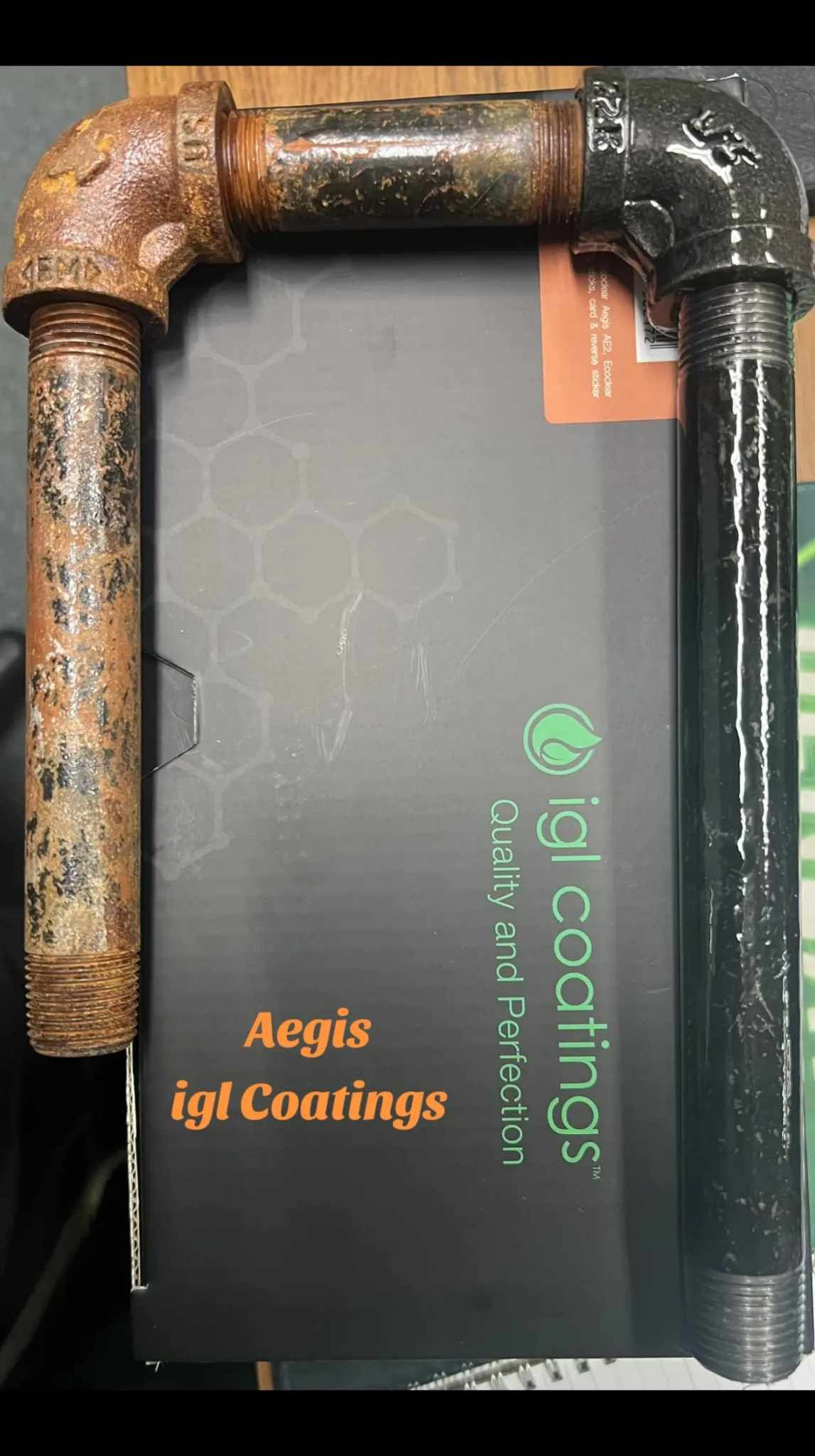 A comparison of a rusted metal pipe assembly next to one treated with a black protective coating on an IGL Coatings box.