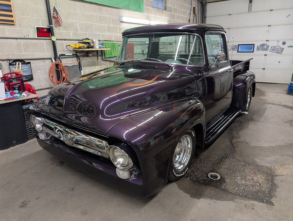 A custom, dark purple vintage pickup truck parked in an indoor garage.