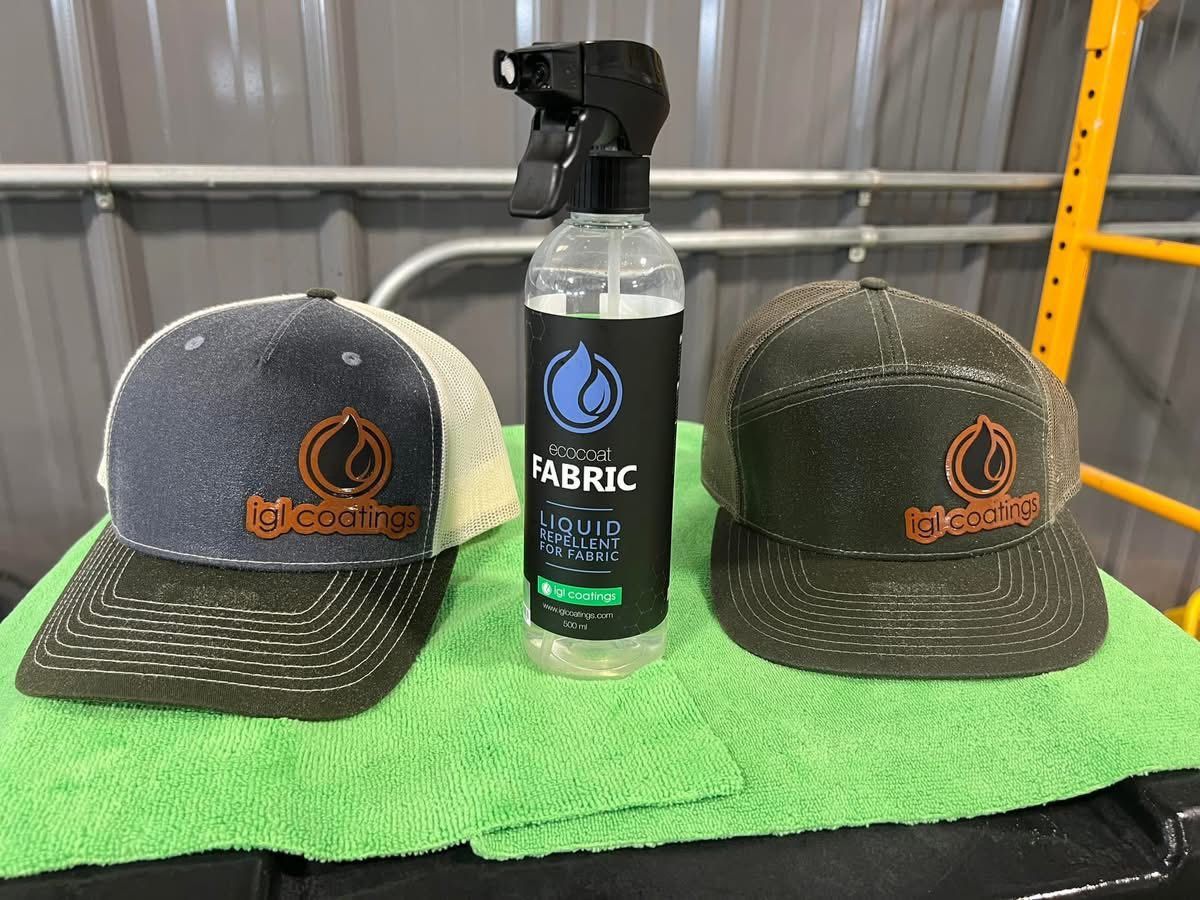 Two baseball caps with a circular logo sit on a green cloth next to a spray bottle labeled 