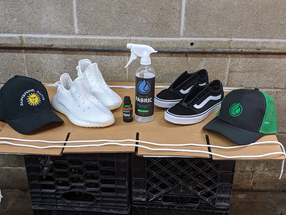 White and black sneakers, two baseball caps, and a cleaning spray bottle displayed on a cardboard surface.