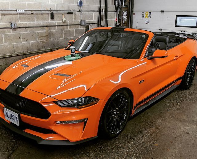 An orange Ford Mustang convertible with black racing stripes parked in a garage.