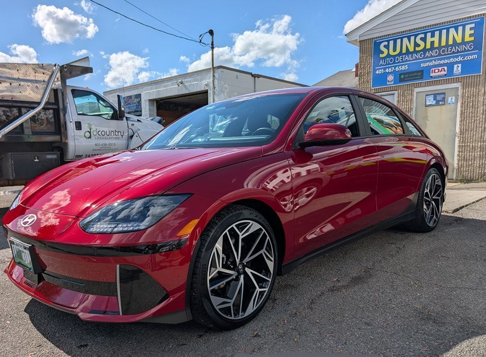 A red Hyundai Ioniq 6 sedan parked in front of a building with a blue