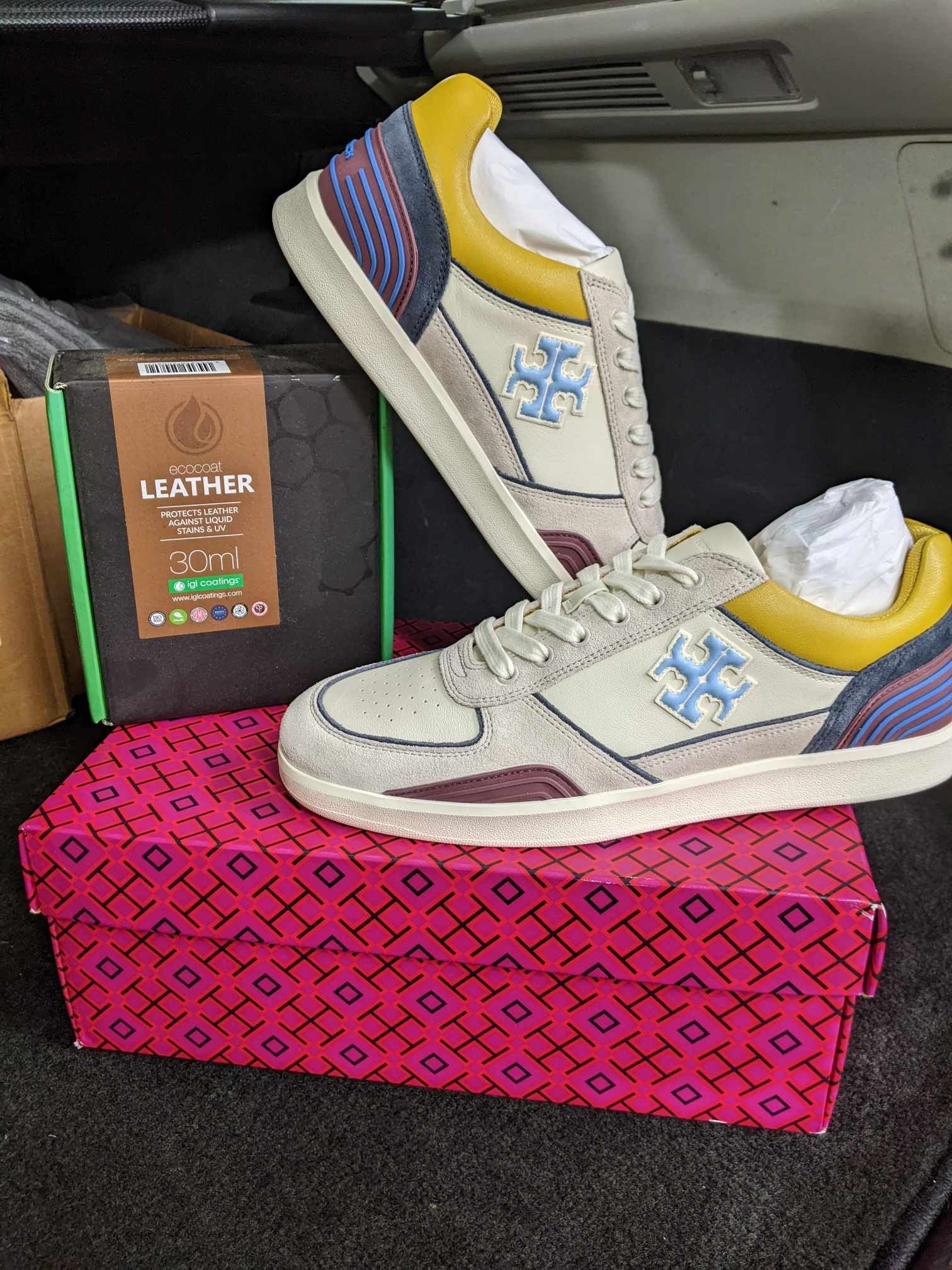 A pair of beige and yellow sneakers with blue logo accents, resting on a patterned pink box next to a box labeled leather.