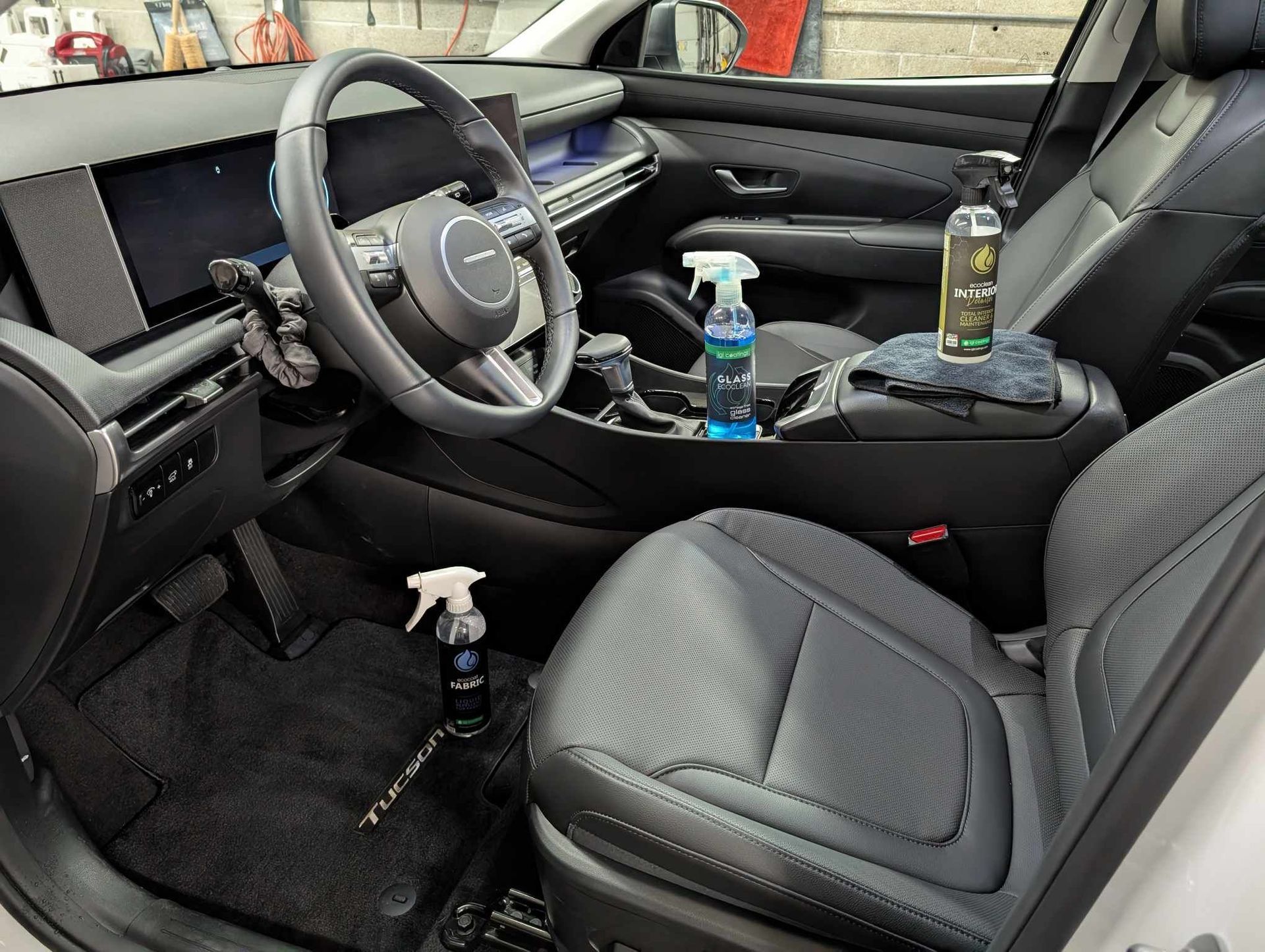 The interior of a clean car with two spray bottles and a cloth used for detailing the dark seats and dashboard.