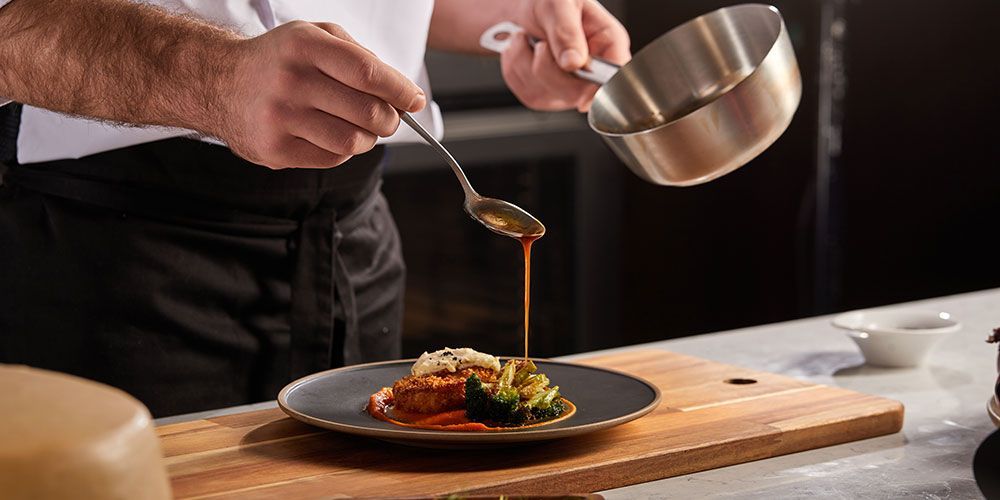 Un chef verse de la sauce sur un morceau de viande dans une assiette