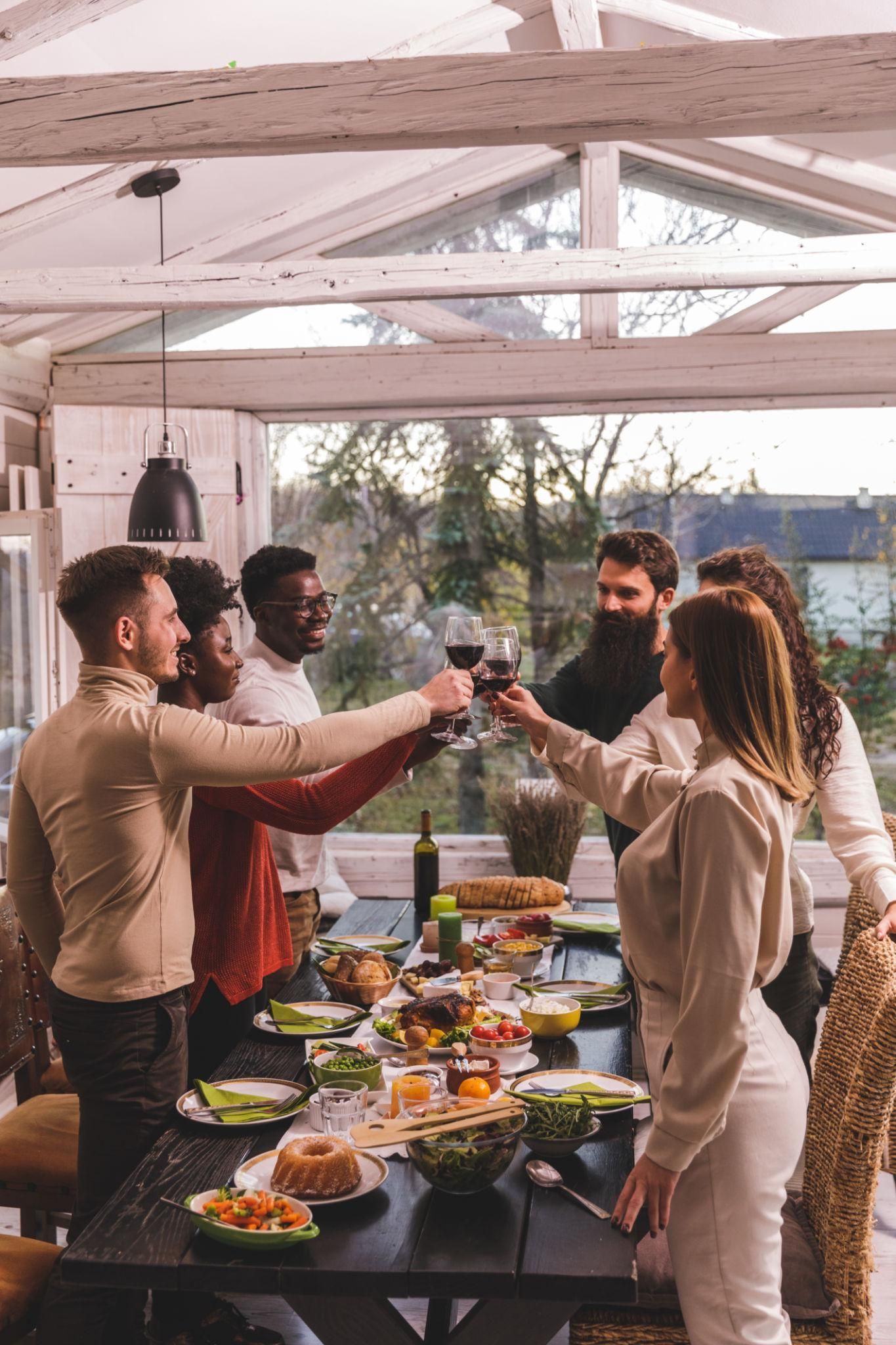Friends toasting with drinks at a long outdoor dinner table under a white pergola