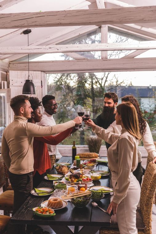 Friends toasting with drinks at a long outdoor dinner table under a white pergola