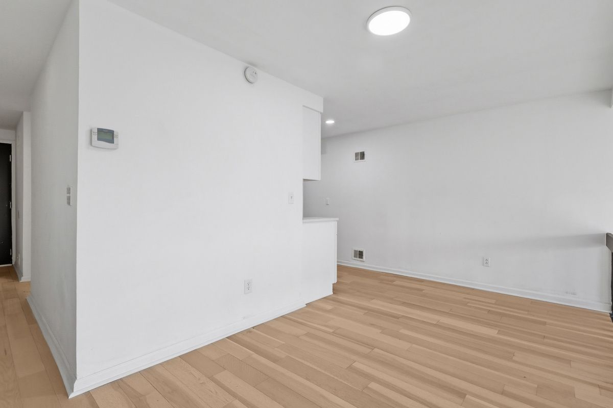 Empty room with white walls, light wood floor, and recessed lighting.