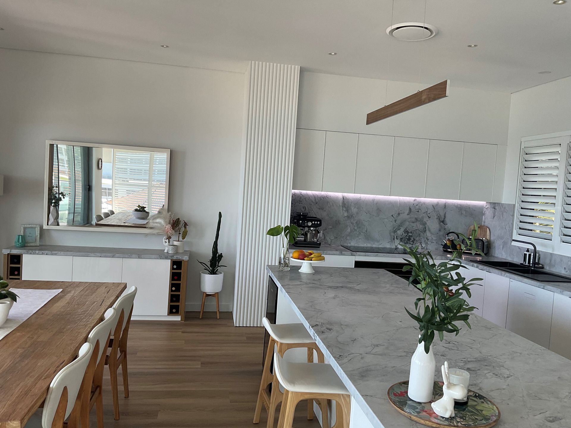 Modern kitchen with a gray island, white cabinets, and a long wooden dining table.