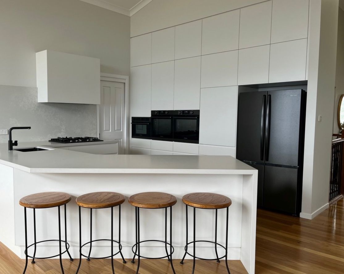 Modern white kitchen with black appliances, a central island with stools, and wooden floors.