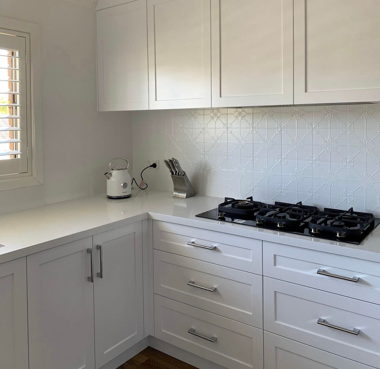 White kitchen with white cabinets, countertop, and geometric backsplash; gas cooktop.