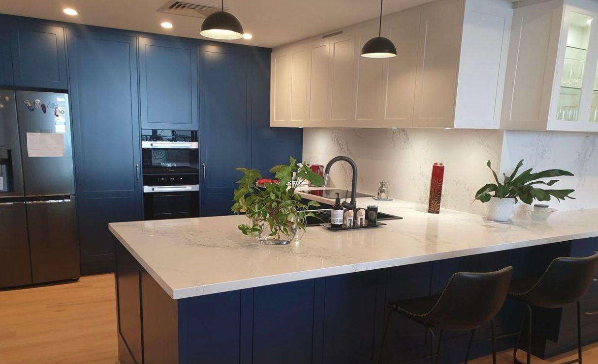 Modern kitchen with navy blue and white cabinets, white countertop, and island with bar stools.