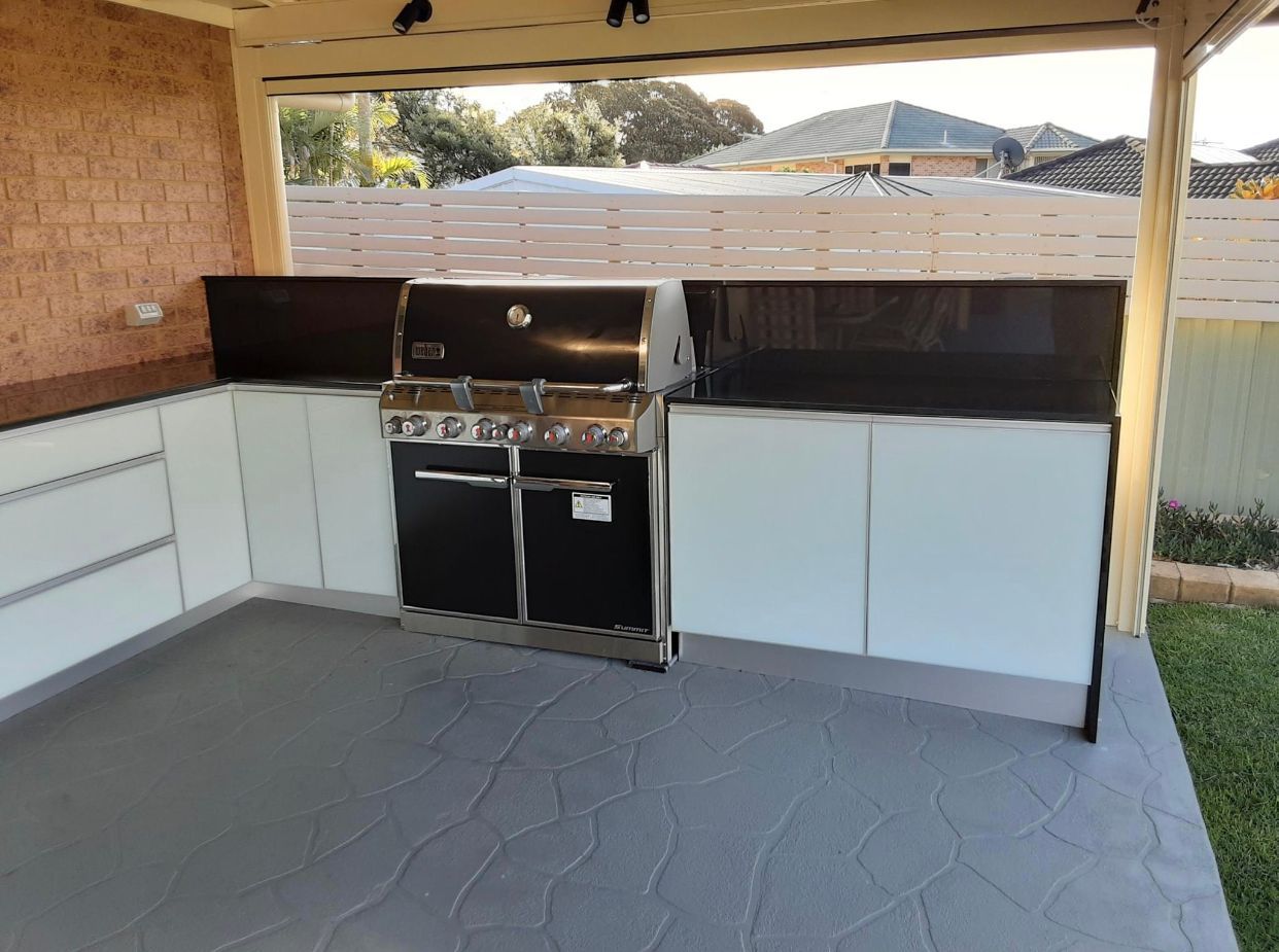 Outdoor kitchen with a grill, cabinets, and a concrete patio.