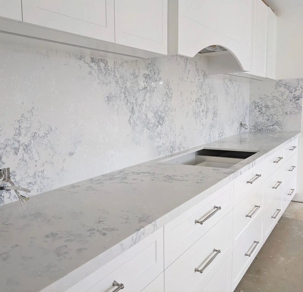 White kitchen with quartz countertops and backsplash, cabinetry with silver hardware.