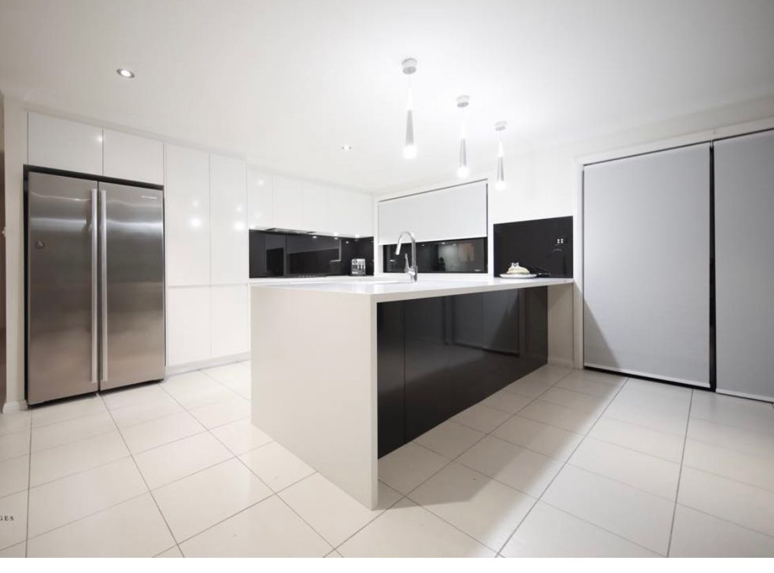 Modern white kitchen with stainless steel fridge, large island, and overhead lighting.