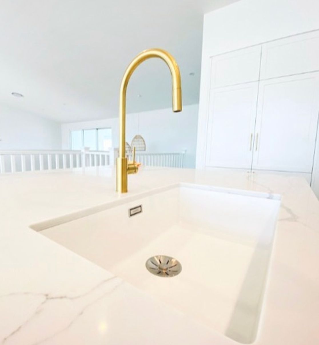 Gold faucet over a white sink in a modern, bright kitchen.