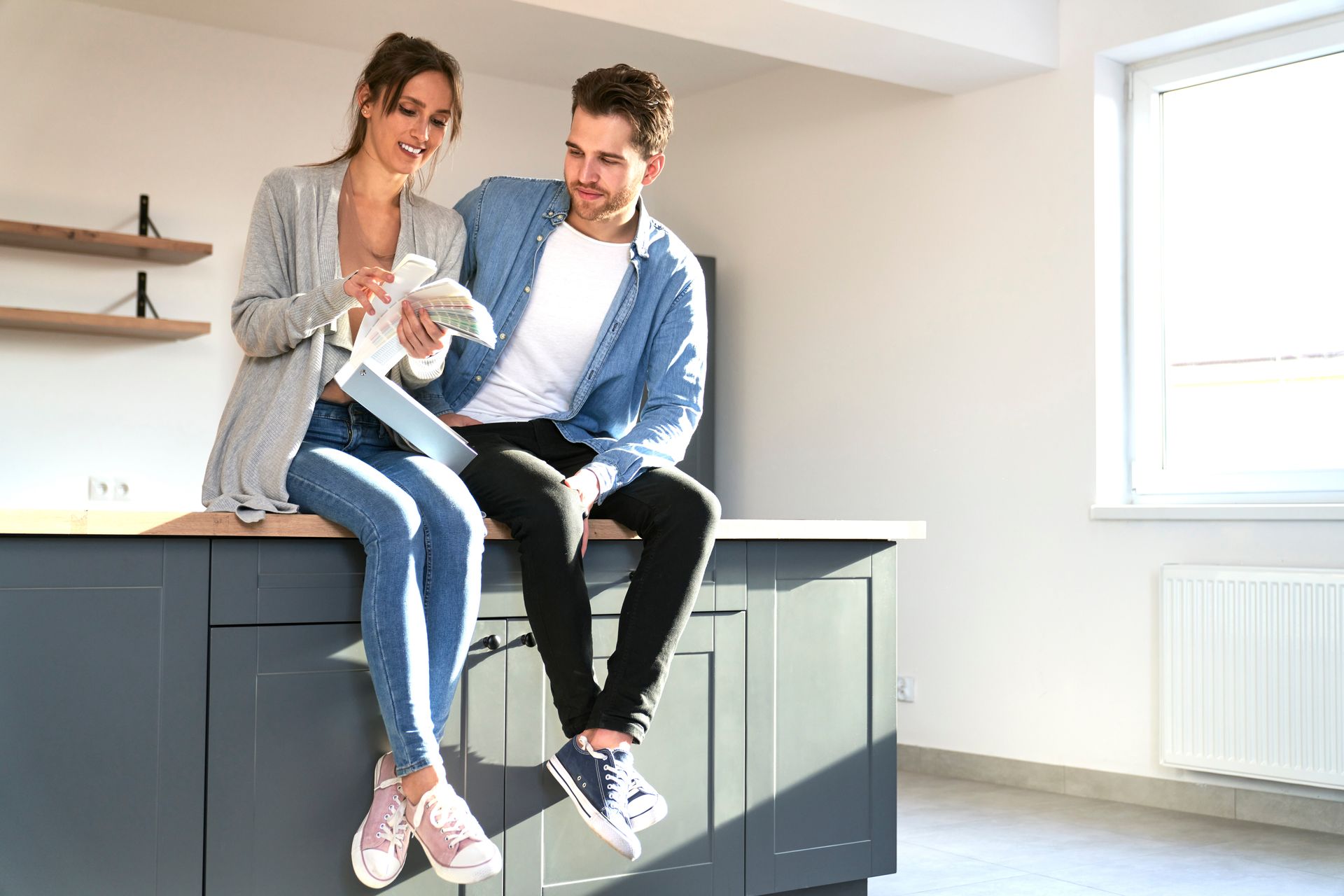 A couple seated on their kitchen island talking and holding a paint palette.