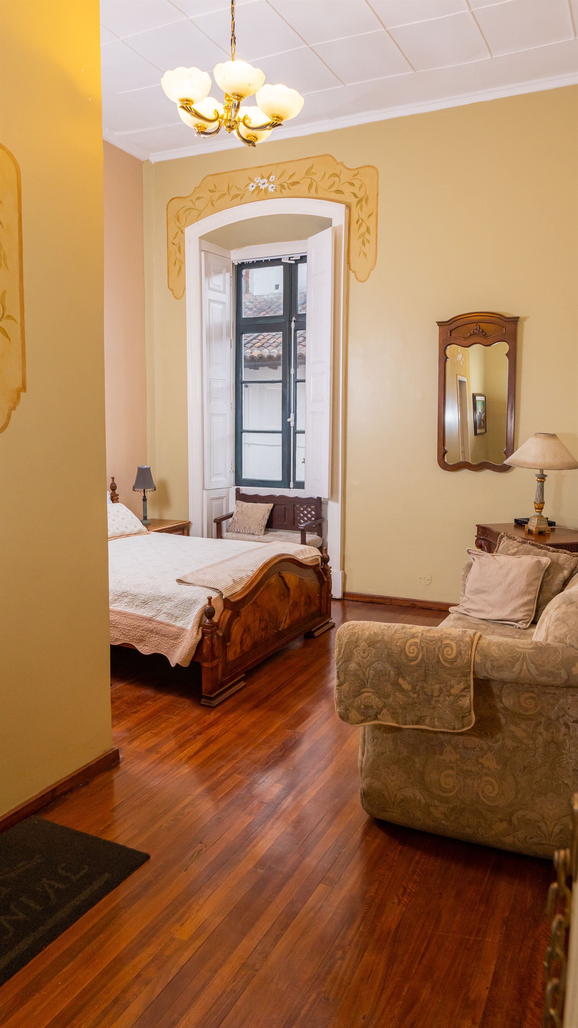 A bedroom with a bed , couch , mirror and window.
