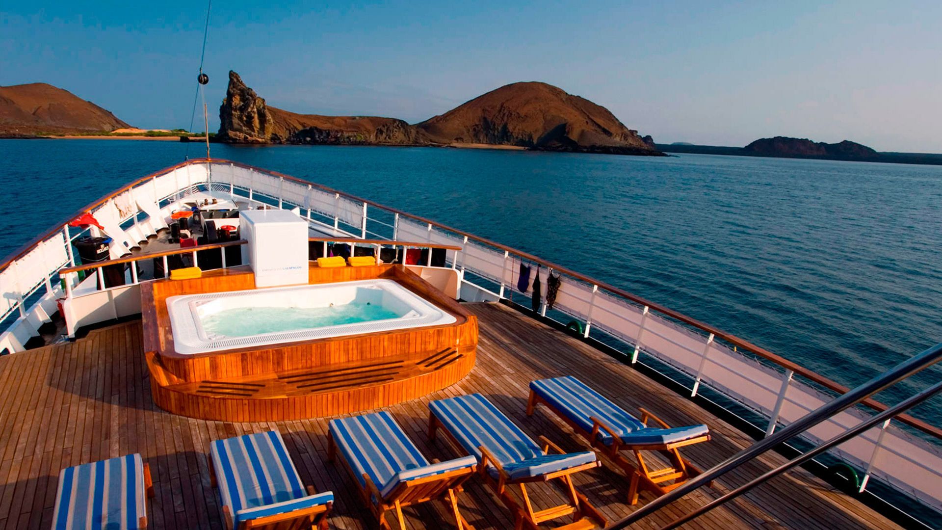 A boat with a jacuzzi on the deck and chairs on the deck.