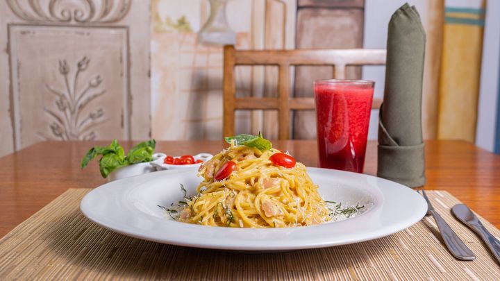 A plate of spaghetti with tomatoes and a glass of juice on a table.