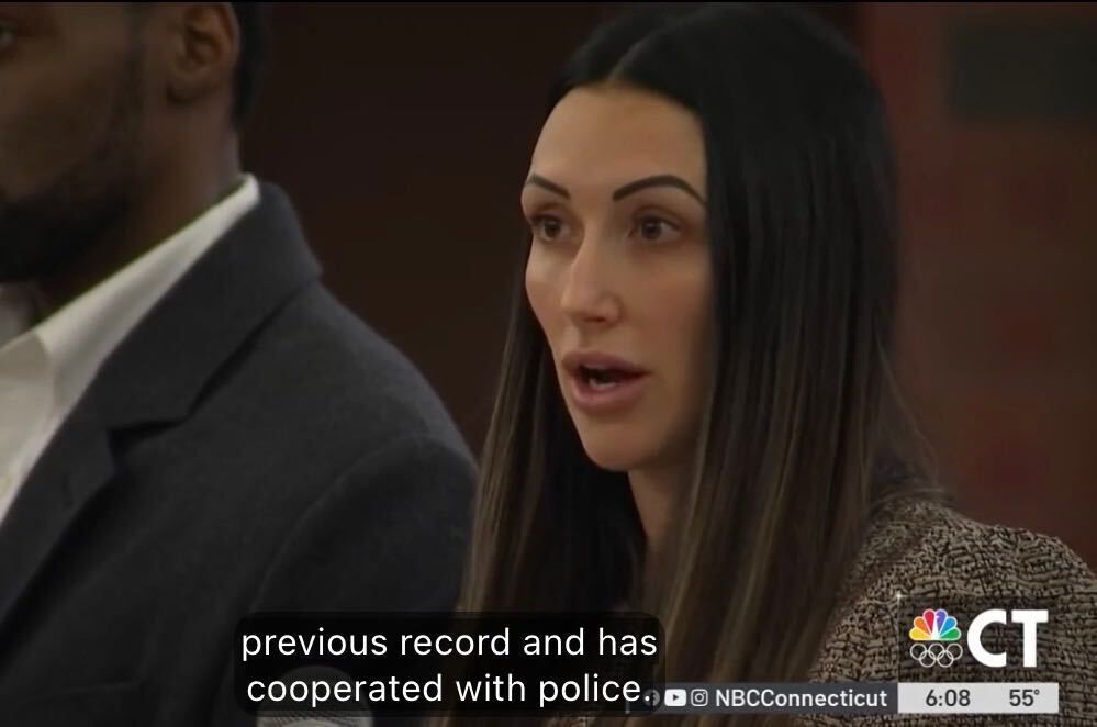 Woman speaking in a meeting room, with a man beside her and TV captions overlaid.