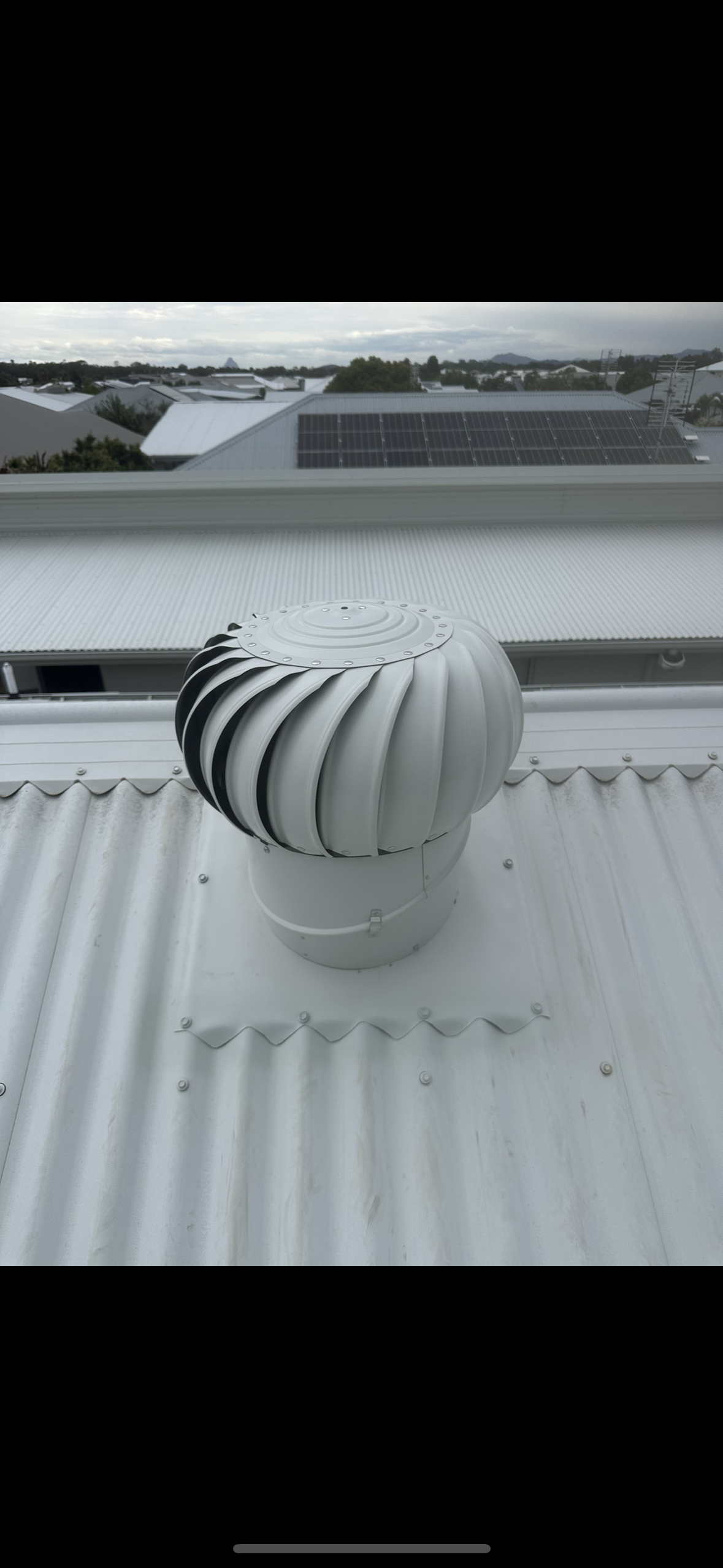 Gray metal tile roof on a house, with a chimney and greenery in the background. — Whirly Bird King in Strathpine, QLD