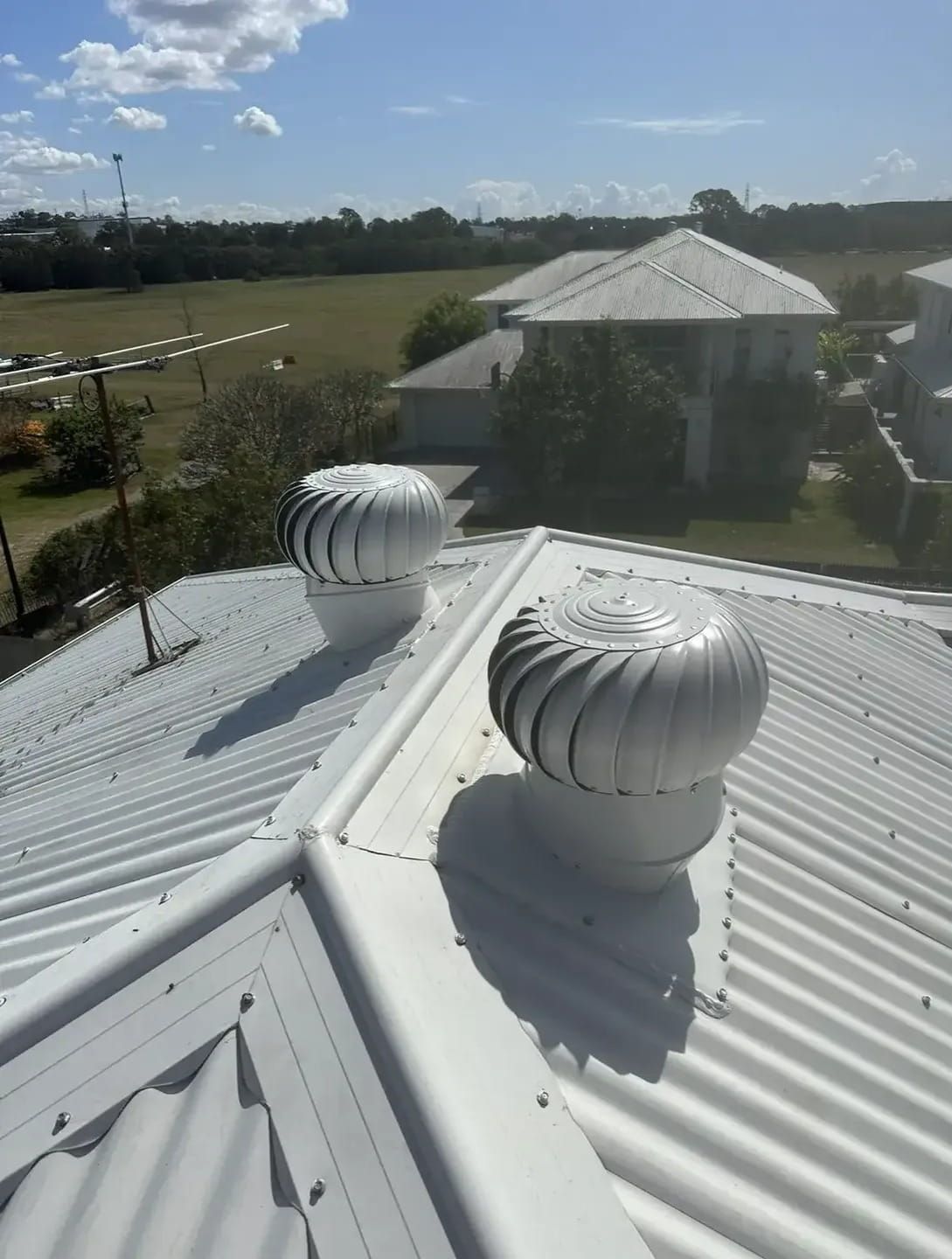 Two White Turbine Roof Vents on a White Corrugated Metal Roof Under a Blue Sky — Whirly Bird King in Mango Hill, QLD