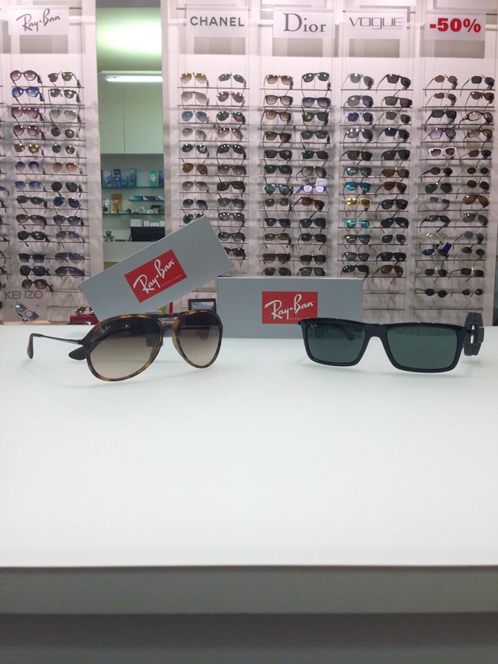 Esposizione di occhiali da sole in un negozio di ottica, con occhiali da sole Ray-Ban in primo piano e pareti con i loghi del marchio sullo sfondo.