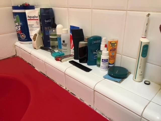 A bathroom counter with a toothbrush , shampoo , lotion , comb , toothpaste and wipes.