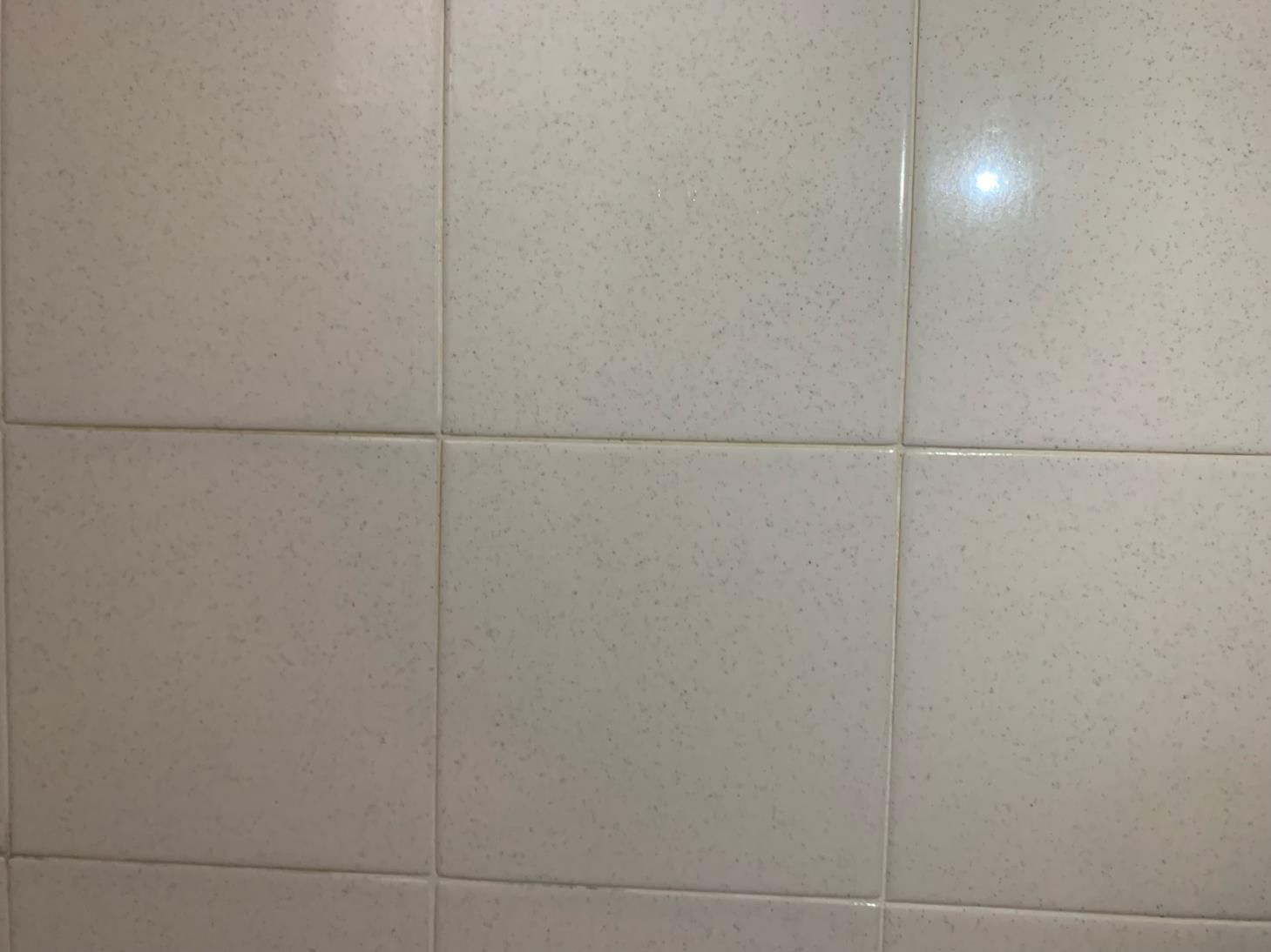 A close up of a white tile wall in a bathroom.