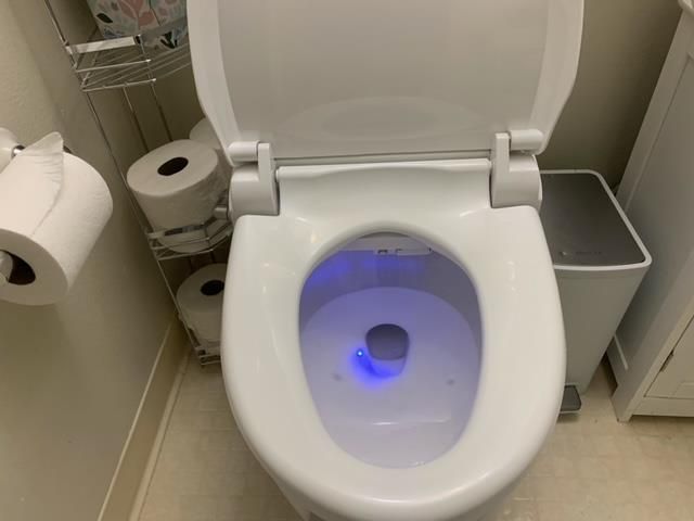 A white toilet with a blue light on the seat in a bathroom.