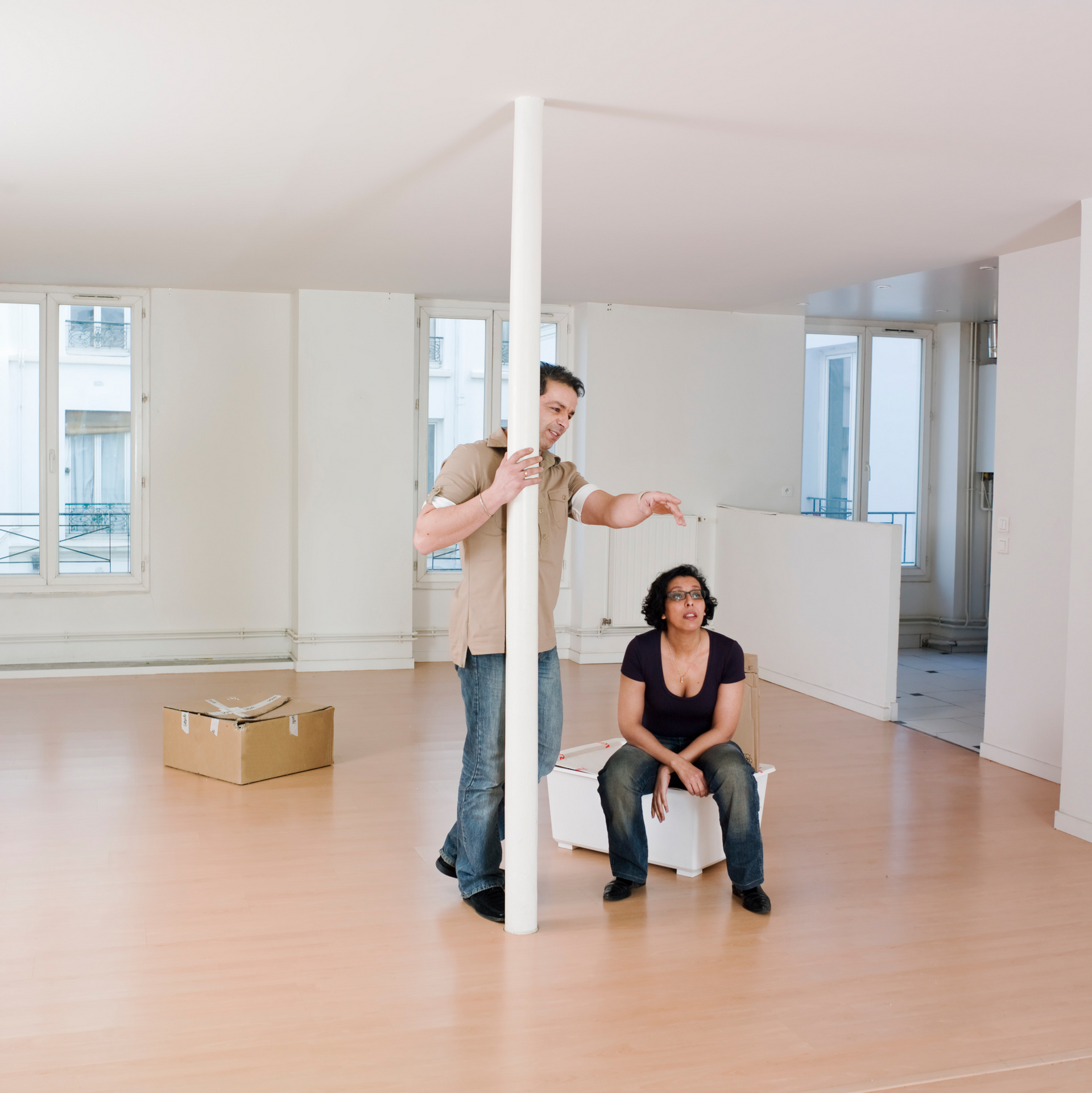 A man standing next to a pole and a woman sitting on a box
