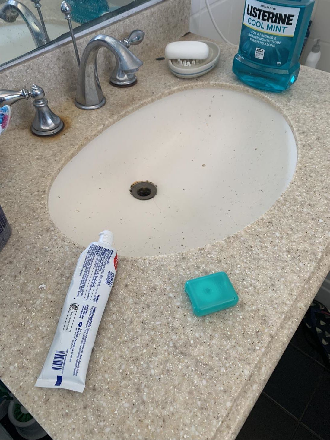 A bathroom sink with a tube of toothpaste and a bottle of listerine mouthwash