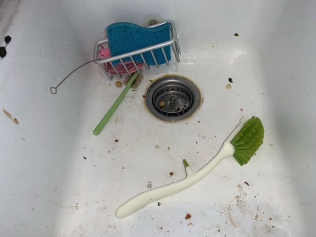A dirty sink with a toothbrush and a sponge in it