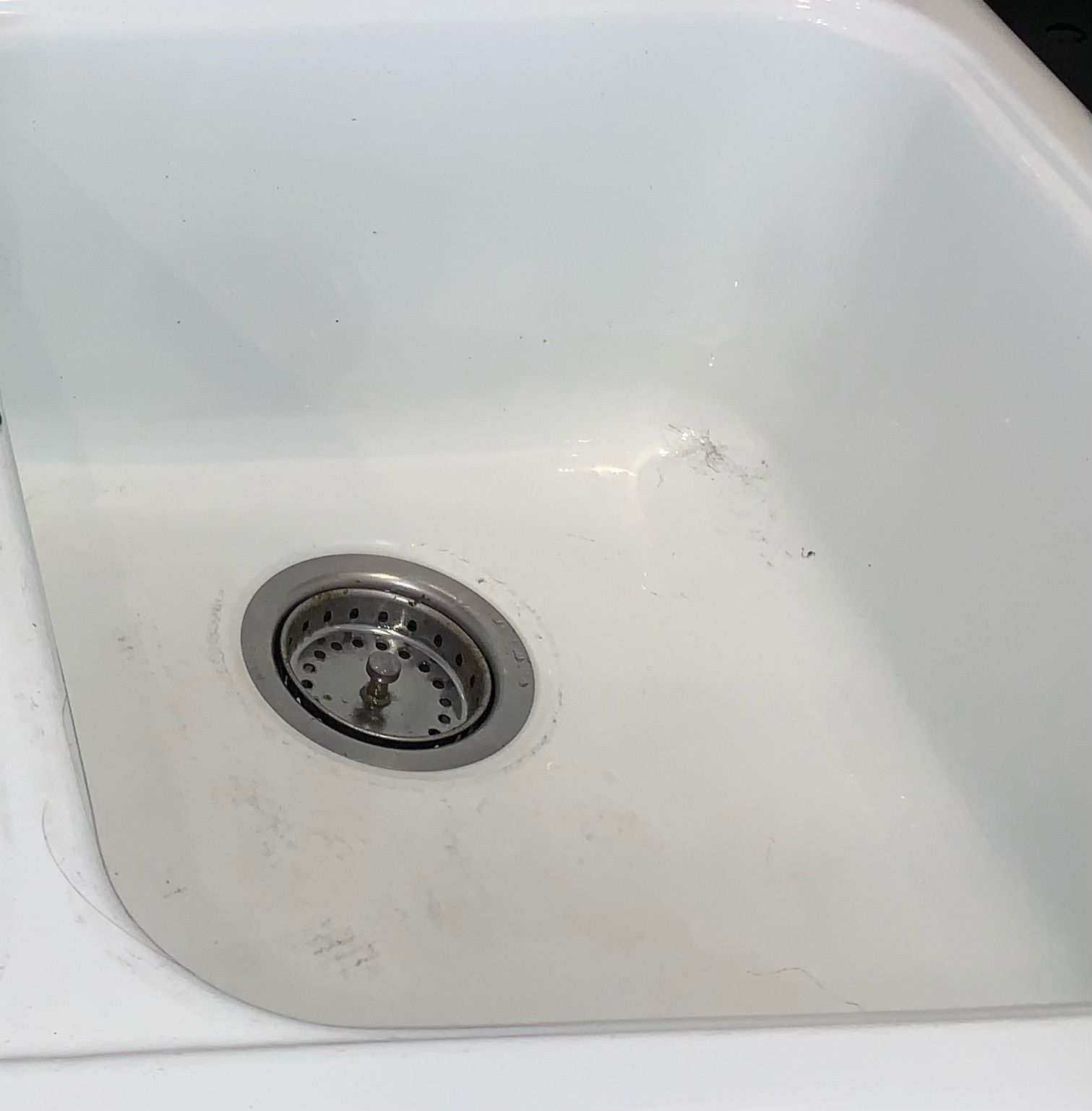 A white kitchen sink with a stainless steel drain