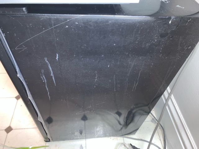 A dirty black refrigerator is sitting on a tiled floor
