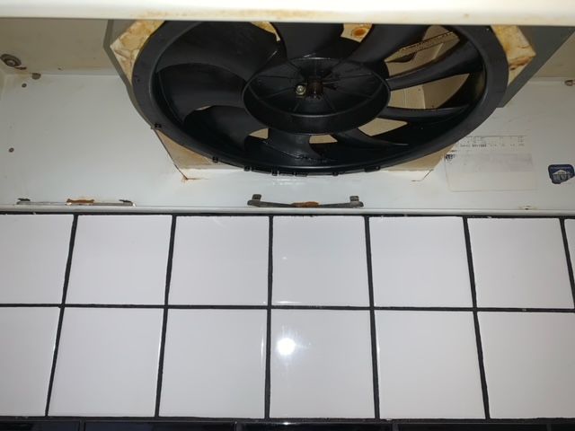 A black fan is mounted to a white tiled wall