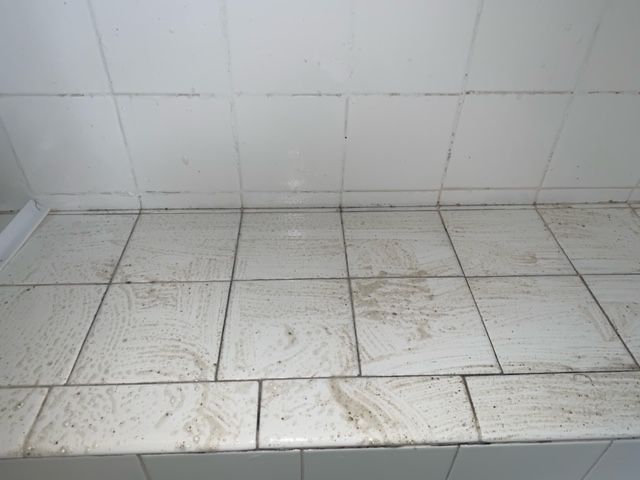 A dirty tile floor in a bathroom with white tiles