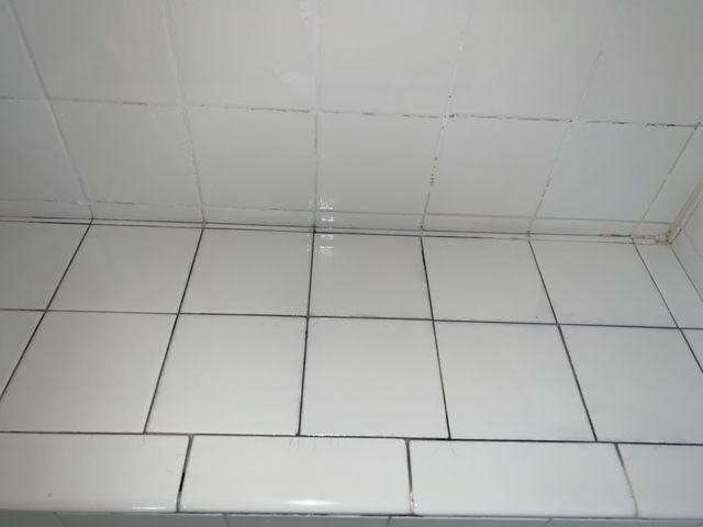 A bathroom floor with white tiles and a white wall