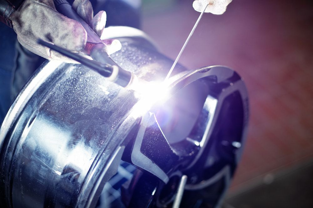 Welder Using a Torch to Repair a Shiny Black Car Rim — LM Engineering in Cooktown, QLD