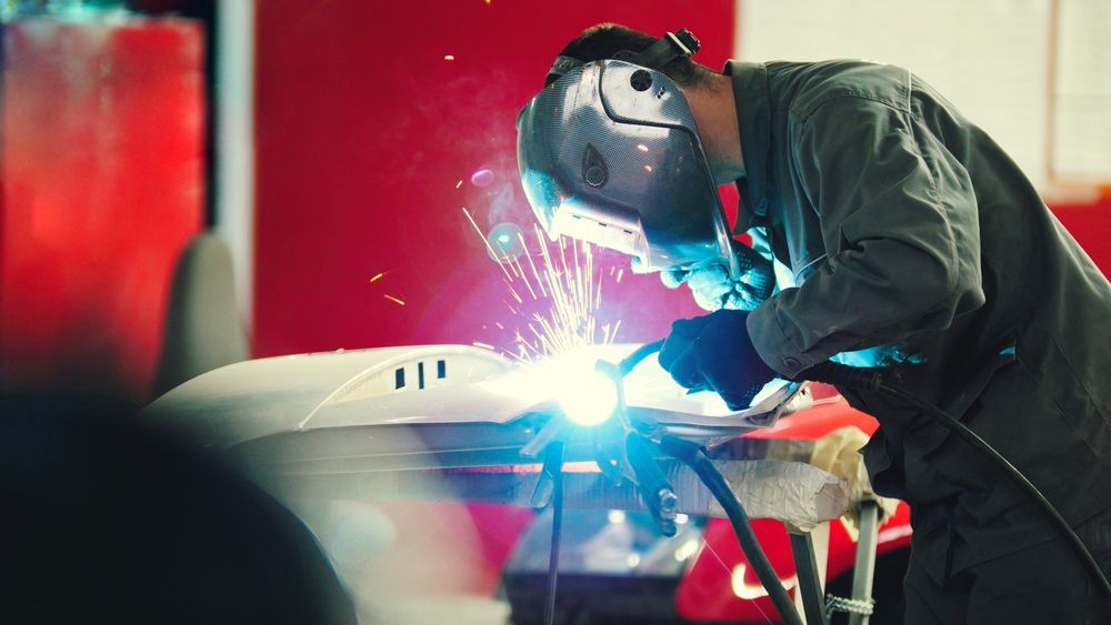 A Man is Welding a Car Hood in a Garage — LM Engineering In Mareeba, QLD