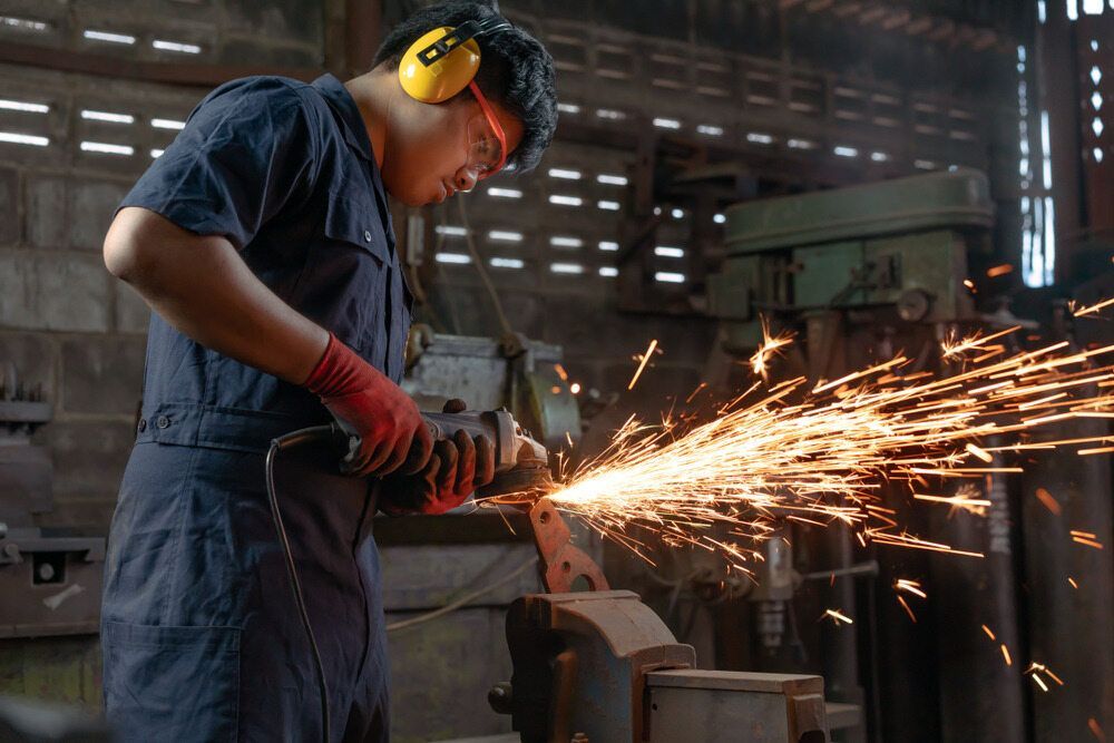 A Man is Grinding a Piece of Metal With a Grinder in a Factory — LM Engineering In Mareeba, QLD