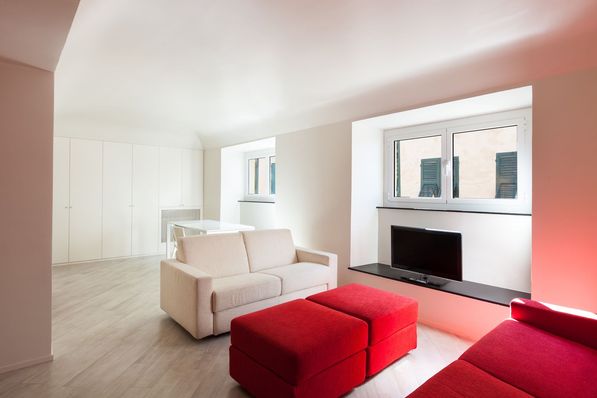 A Living Room With a White Couch and Red Ottomans